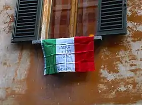 Drapeau tricolore étendu à une fenêtre bolognaise avec les inscriptions « Andrà tutto bene » (« Tout ira bien ») et le mot-clé « Io resto a casa » pendant le confinement de mars 2020.