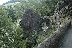 L'image montre une grosse roche accolée à une route, et au milieu de laquelle figure une grande trouée.