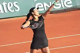 Une joueuse de tennis en robe noir lance la balle en l'air et lève sa raquette pour la frapper.