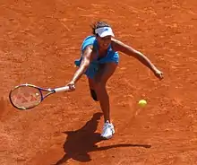 Sur un terrain en terre battue, une joueuse de tennis en bout de course tendant sa raquette pour essayer d'attraper la balle.