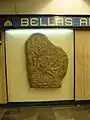 Réplique de pierre tombale exposée au métro Bellas Artes à Mexico. La plaque d'accompagnement est traduisible par "pierre tombale d'Izapa - Culture Maya -  Période préclassique - Description: Original provenant d’Izapa, au Chiapas. Représente un squelette assis avec un (illisible)."