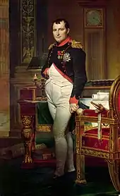  Napoléon debout, une main dans le gilet. Autour de lui, un bureau, un fauteuil, une pendule