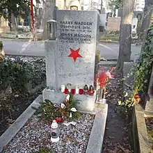 Photographie en couleur d'une tombe, avec des fleurs et des bougies, avec le nom de deux hommes.