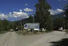 Photographie d'une route de graviers bifurquant dans un paysage montagneux verdoyant sous un ciel bleu intense et légèrement nuageux