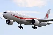 Un Boeing 777 en vol, train d’atterrissage  sortit. Il porte les inscriptions Japan sur le fuselage. Une bande rouge traverse le fuselage de couleur blanche, et un cercle rouge est présent sur la dérive.