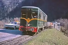 Locomotive verte tractant quelques wagons sur un petit pont au-dessus de la rivière Romanche, également franchi par une route goudronnée.