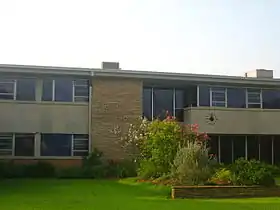 Vue partielle de la façade d'un bâtiment de deux étages avec un bosquet d'arbres près de l'entrée.