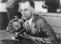 Photographie noir et blanc d'un homme devant un microphone radiophonique.