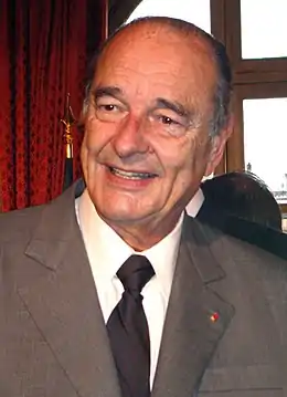 Photographie en couleurs de Jacques Chirac, en 2006. L'image cadre son buste et son visage, souriant.