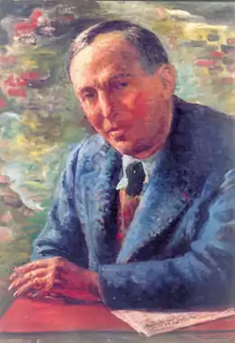 Portrait d’un homme en veste bleue, appuyé sur une table rouge.