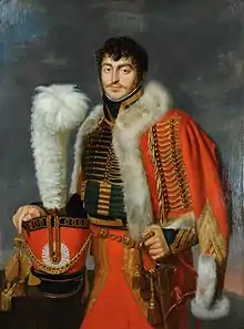 Portrait à mi-jambes d'un officier de Napoléon, vêtu d'un veste verte et portant sur l'épaule un grand manteau rouge bordé de fourrure blanche, posant sa main sur sa coiffe à plumet blanc, à gauche.