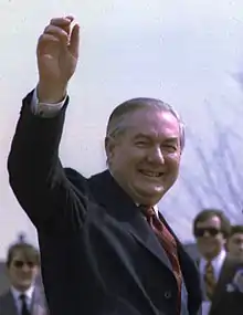 Un homme en costume et cravate lève le bras d'un air enjoué et victorieux.