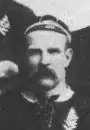 Photo en buste d'un joueur moustachu. Il porte un maillot noir et un bonnet