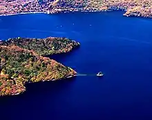 Photo couleur d'un îlot dans une étendue d'eau couleur bleu de cobalt. La rive boisée du lac en arrière-plan.