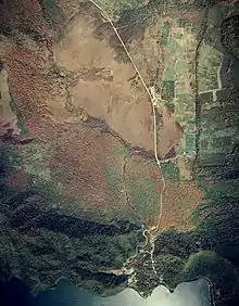 Photo couleur d'une voie routière traversant une plaine herbeuse entourée d'espaces forestiers.