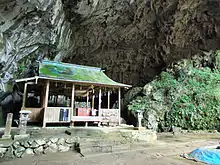 Photo couleur d'un édifice religieux en bois à l'entrée d'une grotte.