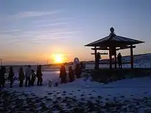 Photo couleur d'un lever de soleil vu du bord d'une plage enneigée.