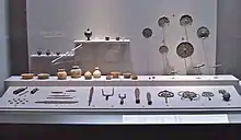 Photo couleur d'objets anciens (poteries, outils, ornements religieux) exposés derrière une vitrine.
