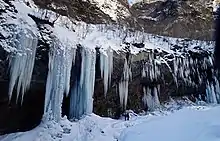 Photo couleur de stalactites de glace le long d'une paroi rocheuse enneigée.