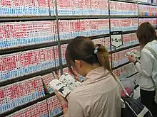 Photographie d'un rayonnage de livres dans un magasin, avec deux lectrices qui lisent devant.