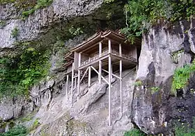 Une structure en bois sur une falaise soutenue par de longues perches en bois.