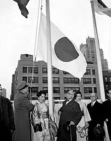 Un groupe d'hommes et femmes regardant un drapeau se faisant hisser.