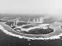 Photo en noir et blanc d'une île d'où s'élèvent des colonnes de fumées.