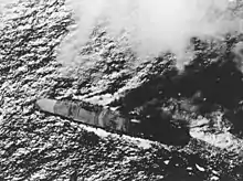 Photo en noir et blanc d'un porte-avions en flammes, vu du dessus