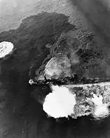 Photographie en noir et blanc prise d'un avion à basse altitude montrant un bateau subissant un bombardement.