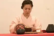 Une femme vêtue d’un habit traditionnel japonais. Devant elle, une théière et un plateau.