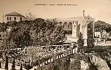 Vue aérienne du jardin et de la chapelle, avec au fond un bâtiment à colonnade et le dôme d'une cathédrale.