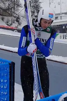 un homme avec la tête baissée et des skis sur l'épaule