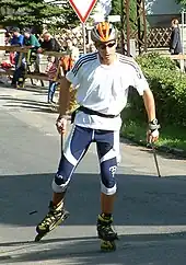 Portrait de Jason Lamy-Chappuis sur des rollers, portant un casque orange, des lunettes, un maillot blanc et un pantalon bleu.