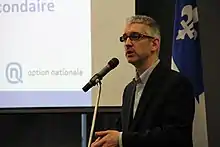 Photo de Jean-Martin Aussant alors qu'il parle au micro lors d'une assemblée.