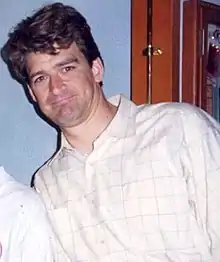 Photographie en couleur d'un jeune homme en t-shirt blanc souriant.