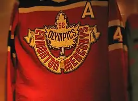 Un maillot rouge avec des bandes noires. Une feuille d'érable et les mots Edmonton Mercurys et 52 Olympics y figurent.