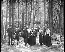 Photographie de participants à un jeu de boules dans le bois de Rambouillet. Dix personnes, dont six femmes, deux hommes et deux enfants posent.