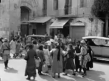 Photographie en noir et blanc, montrant une foule de personnes guidées par des soldats armés.