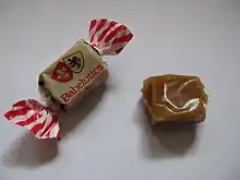Photographie en couleurs de deux bonbons au caramel, l'un encore emballé dans son papier.