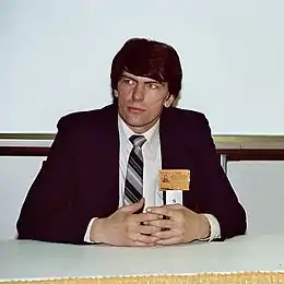 photographie couleur d'un homme assis derrière une table