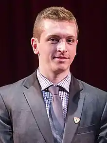 Un jeune homme en costume-cravate avec un léger sourire.