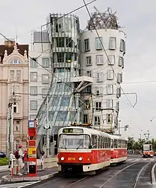 Un vieux tramway rouge et crème au premier plan devant un bâtiment très moderne de verre et de béton.