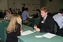 photo d'une salle où des personnes sont assises face à face sur plusieurs tables.