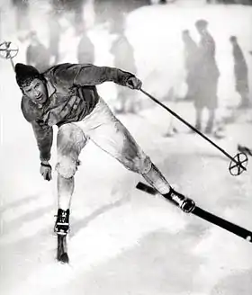 Photographie en noir et blanc d'un homme pratiquant le ski de fond, le corps penché en avant, en équilibre sur le ski droit.