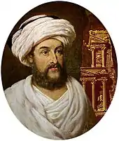 Gravure d'un homme barbu habillé d'un turban blanc et d'un vêtement blanc de bebouin. L'arrière plan est occupé par la un monument sculpté dans la roche