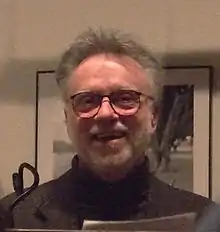 Photo d'un homme barbu et souriant faisant face à la caméra.