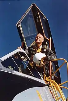 Photo de John Glenn se penchant d'un cockpit et regardant au loin.