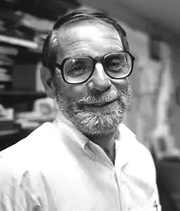 Visage d'un homme portant lunettes, barbu et souriant.