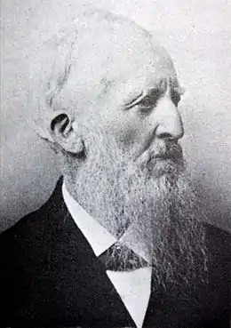 Photographie en noir et blanc du visage d'une homme âgée portant une longue barbe, vu de profil droit