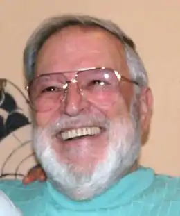 photographie en couleur d'un homme avec lunettes, moustaches et barbe blanche souriant